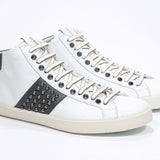 Dreiviertelansicht der Vorderseite von Mid Top weiß und militärgrün sneaker. Obermaterial aus Vollleder mit Nieten, einem internen Reißverschluss und einer Vintage-Gummisohle.