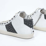 Dreiviertelansicht der Rückseite von Mid Top weiß und militärisch grün sneaker. Obermaterial aus Vollleder mit Nieten, einem internen Reißverschluss und einer Vintage-Gummisohle.