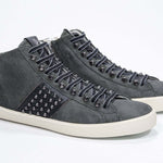 Dreiviertelansicht der Vorderseite von Mid Top Military Green sneaker. Obermaterial aus Wildleder und Leder mit Nieten, einem internen Reißverschluss und einer Vintage-Gummisohle.
