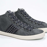 Dreiviertelansicht der Vorderseite von Mid Top Military Green sneaker. Obermaterial aus Wildleder und Leder mit Nieten, einem internen Reißverschluss und einer Vintage-Gummisohle.