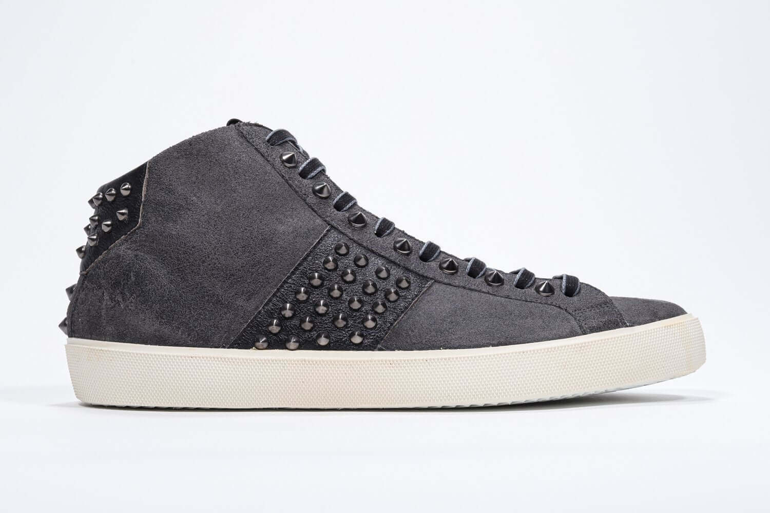 Profilo laterale di mid top grigio scuro sneaker. Tomaia in pelle e camoscio con borchie, zip interna e suola in gomma vintage.