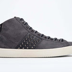 Profilo laterale di mid top grigio scuro sneaker. Tomaia in pelle e camoscio con borchie, zip interna e suola in gomma vintage.