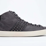 Profilo laterale di mid top grigio scuro sneaker. Tomaia in pelle e camoscio con borchie, zip interna e suola in gomma vintage.
