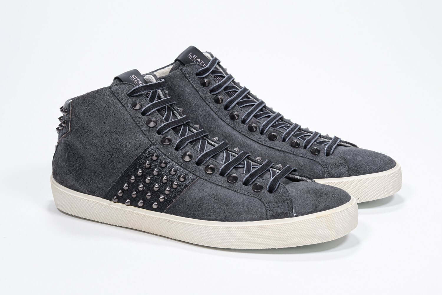 Vista frontale di tre quarti del modello mid top grigio scuro sneaker. Tomaia in pelle e camoscio con borchie, zip interna e suola in gomma vintage.