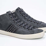 Vista frontale di tre quarti del modello mid top grigio scuro sneaker. Tomaia in pelle e camoscio con borchie, zip interna e suola in gomma vintage.