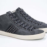Vista frontale di tre quarti del modello mid top grigio scuro sneaker. Tomaia in pelle e camoscio con borchie, zip interna e suola in gomma vintage.