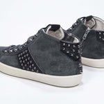 Vista posteriore di tre quarti del modello mid top grigio scuro sneaker. Tomaia in pelle e camoscio con borchie, zip interna e suola in gomma vintage.