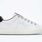 Profil latéral de la chaussure blanche sneaker avec des détails noirs et le logo perforé de la couronne sur la tige. Tige en cuir et semelle en caoutchouc blanc.