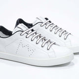 Vue de trois quarts avant de la chaussure blanche sneaker avec des détails noirs et un logo perforé sur la tige. Tige en cuir et semelle en caoutchouc blanc.