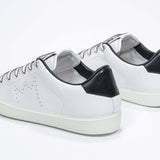 Vue de trois quarts arrière de la chaussure blanche sneaker avec des détails noirs et le logo perforé de la couronne sur la tige. Tige en cuir et semelle en caoutchouc blanc.