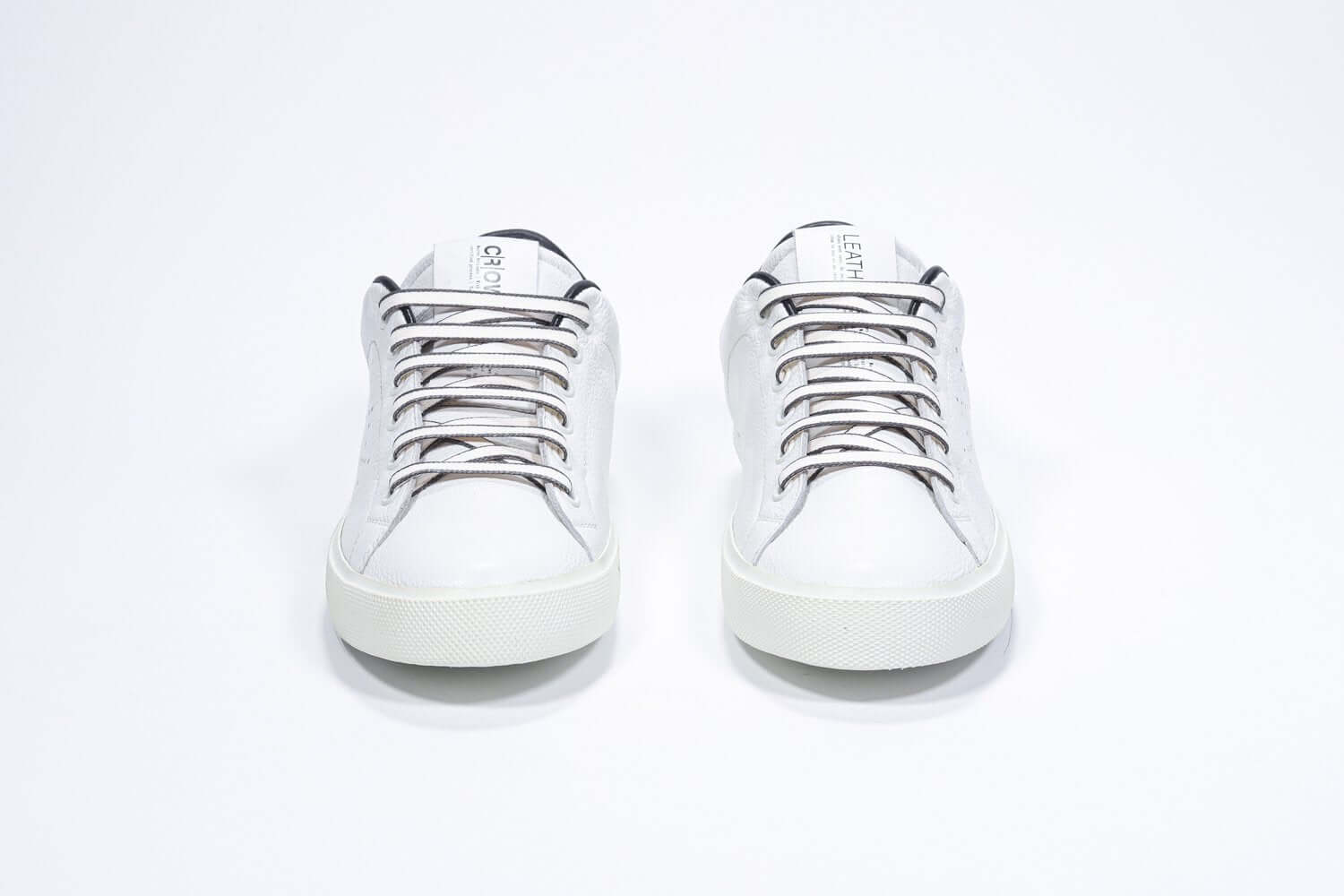 Vue de face de la chaussure blanche sneaker avec des détails noirs et le logo perforé de la couronne sur l'empeigne. Tige en cuir et semelle en caoutchouc blanc.