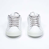 Vue de face de la chaussure blanche sneaker avec des détails noirs et le logo perforé de la couronne sur l'empeigne. Tige en cuir et semelle en caoutchouc blanc.