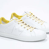 Three quarter front view of low top white sneaker with yellow detailing and perforated crown logo on upper. Full leather upper and white rubber sole.