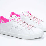 Vue de trois quarts avant de la chaussure basse blanche sneaker avec des détails rose néon et le logo perforé de la couronne sur la tige. Tige en cuir et semelle en caoutchouc blanc.