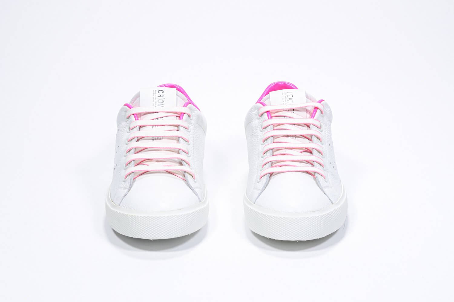 Vue de face de la chaussure blanche sneaker avec des détails rose néon et le logo perforé de la couronne sur la tige. Tige en cuir et semelle en caoutchouc blanc.