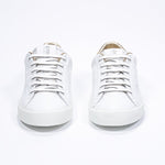 Vue de face de la chaussure blanche sneaker avec des détails dorés et le logo perforé de la couronne sur l'empeigne. Tige en cuir et semelle en caoutchouc blanc.