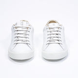 Vue de face de la chaussure blanche sneaker avec des détails dorés et le logo perforé de la couronne sur l'empeigne. Tige en cuir et semelle en caoutchouc blanc.