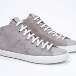 Three quarter front view of mid top beige sneaker with full suede upper with perforated crown logo, internal zip and white sole.