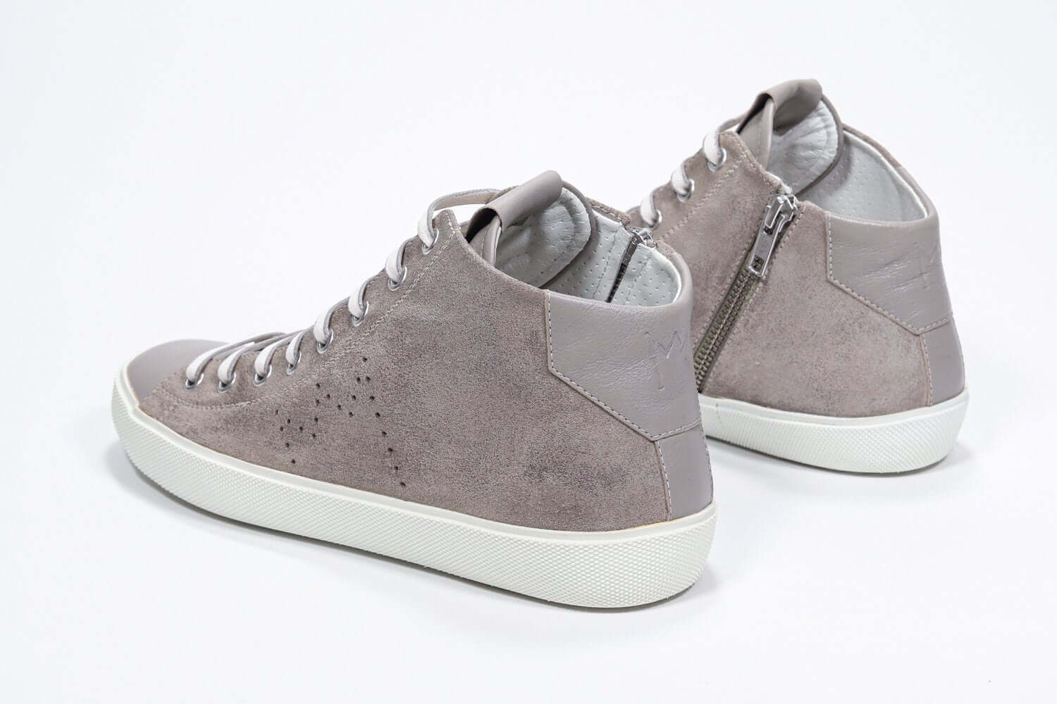 Three quarter back view of mid top beige sneaker with full suede upper with perforated crown logo, internal zip and white sole.