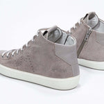 Three quarter back view of mid top beige sneaker with full suede upper with perforated crown logo, internal zip and white sole.