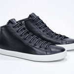 Three quarter front view of mid top black sneaker with full leather upper with perforated crown logo, internal zip and white sole.