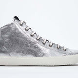 Profil latéral d'un modèle intermédiaire argenté sneaker avec une tige en cuir avec un logo perforé, une fermeture éclair interne et une semelle blanche.