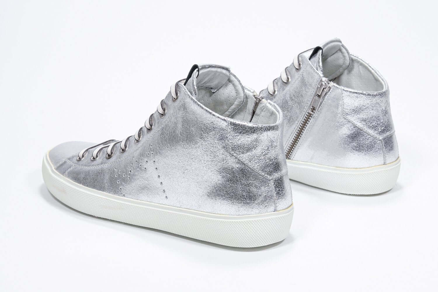 Vue de trois quarts arrière d'un modèle argenté de taille moyenne sneaker avec une tige en cuir avec un logo perforé, une fermeture à glissière interne et une semelle blanche.
