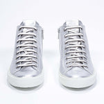 Vue de face du modèle mid top argenté sneaker avec une tige en cuir avec un logo perforé, une fermeture éclair interne et une semelle blanche.