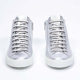 Vue de face du modèle mid top argenté sneaker avec une tige en cuir avec un logo perforé, une fermeture éclair interne et une semelle blanche.