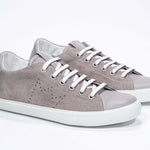 Vue de trois quarts de l'avant de la chaussure beige sneaker avec le logo perforé de la couronne sur l'empeigne. Tige en daim et semelle en caoutchouc blanc.