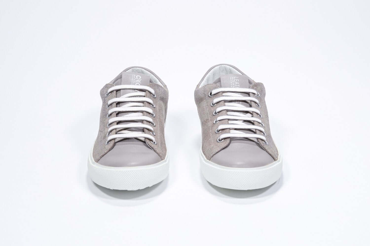 Vue de face de la chaussure beige sneaker avec le logo perforé de la couronne sur la tige. Tige en daim et semelle en caoutchouc blanc.