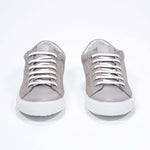 Vue de face de la chaussure beige sneaker avec le logo perforé de la couronne sur la tige. Tige en daim et semelle en caoutchouc blanc.