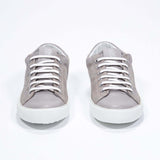 Vue de face de la chaussure beige sneaker avec le logo perforé de la couronne sur la tige. Tige en daim et semelle en caoutchouc blanc.