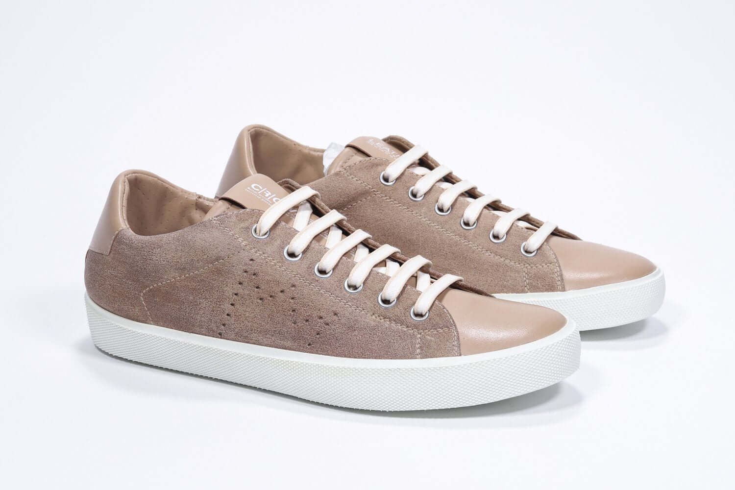 Vue de trois quarts avant de la chaussure basse cuoio sneaker avec le logo perforé de la couronne sur la tige. Tige en daim et semelle en caoutchouc blanc.