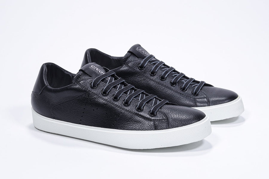 Three quarter front view of low top black sneaker with perforated crown logo on upper. Full leather upper and white rubber sole.