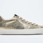 Seitliches Profil des goldenen Low Top sneaker mit perforiertem Kronenlogo auf dem Obermaterial. Obermaterial aus Metallic-Leder und weiße Gummisohle.