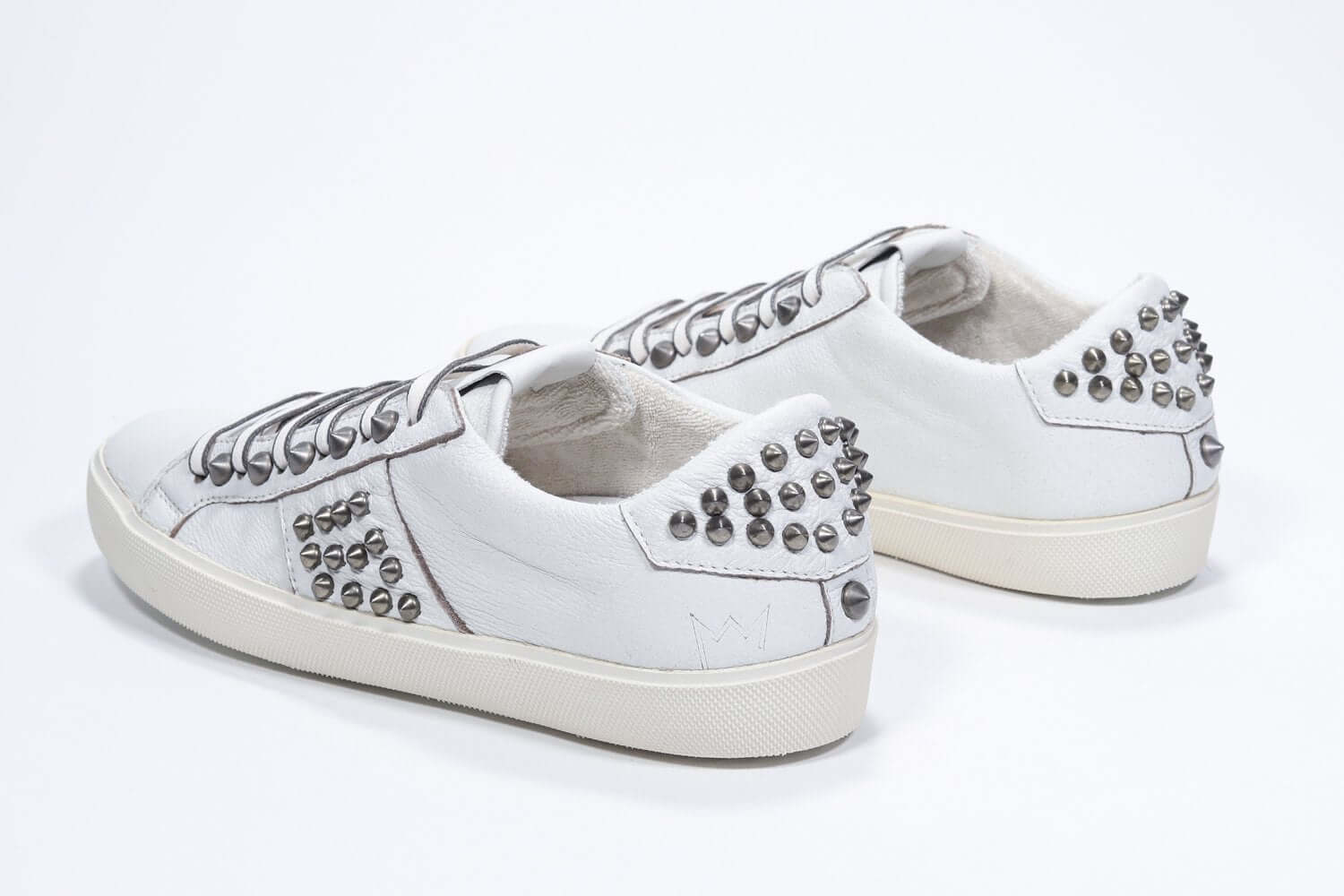 Vue de trois quarts arrière d'une chaussure blanche sneaker. Tige en cuir avec clous et semelle en caoutchouc vintage.