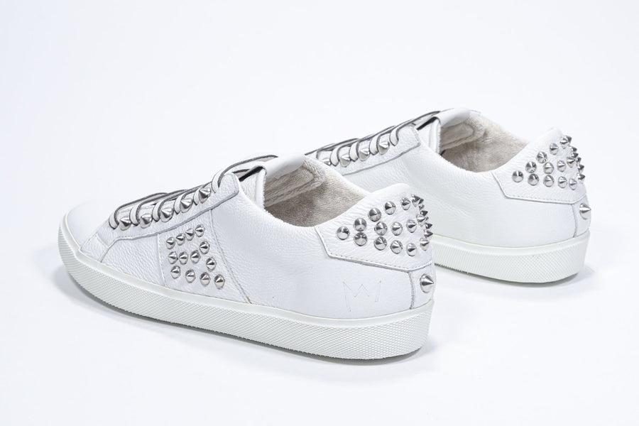 Three quarter back view of low top white sneaker. Full leather upper with studs and white rubber sole.