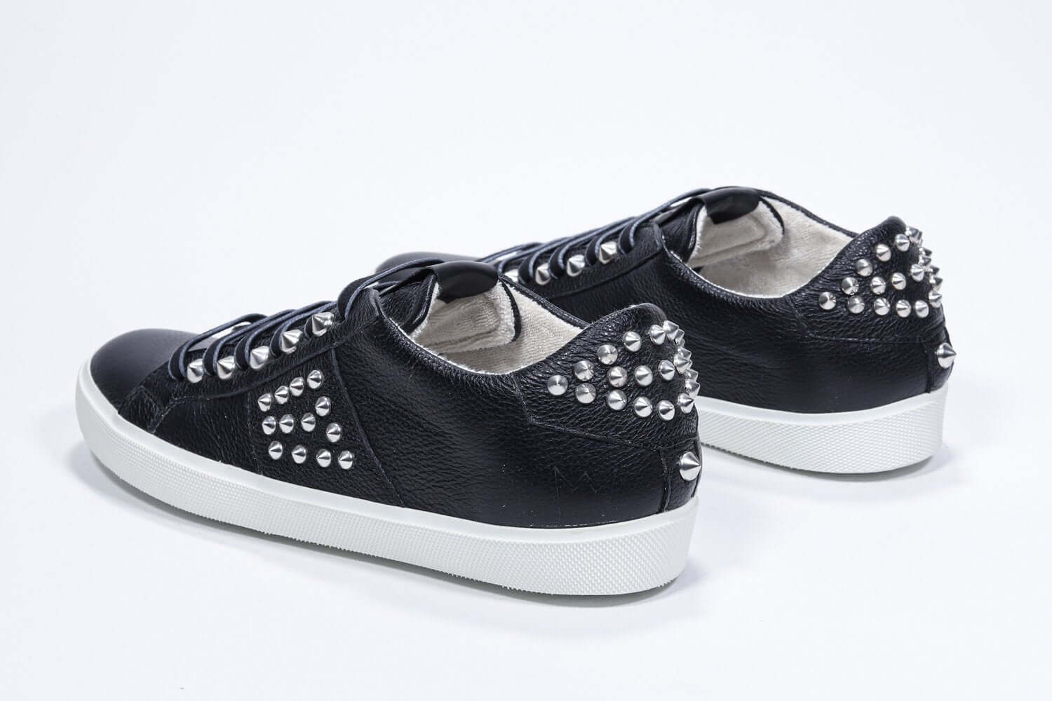 Three quarter back view of low top black sneaker. Full leather upper with studs and white rubber sole.