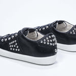 Three quarter back view of low top black sneaker. Full leather upper with studs and white rubber sole.