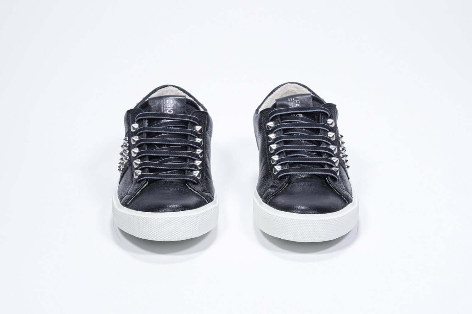 Front view of low top black sneaker. Full leather upper with studs and white rubber sole.