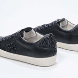Vue de trois quarts arrière d'un modèle bas noir sneaker. Tige en cuir avec clous et semelle en caoutchouc vintage.