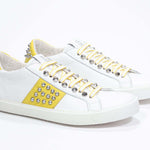 Dreiviertelansicht der Vorderseite von Low Top weiß und gelb sneaker. Obermaterial aus Vollleder mit Nieten und weißer Gummisohle.