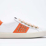 Profilo laterale di BASSE bianco e arancione sneaker. Tomaia in pelle con borchie e suola in gomma vintage.
