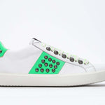 Side profile of low top white and neon green sneaker. Full leather upper with studs and white rubber sole.