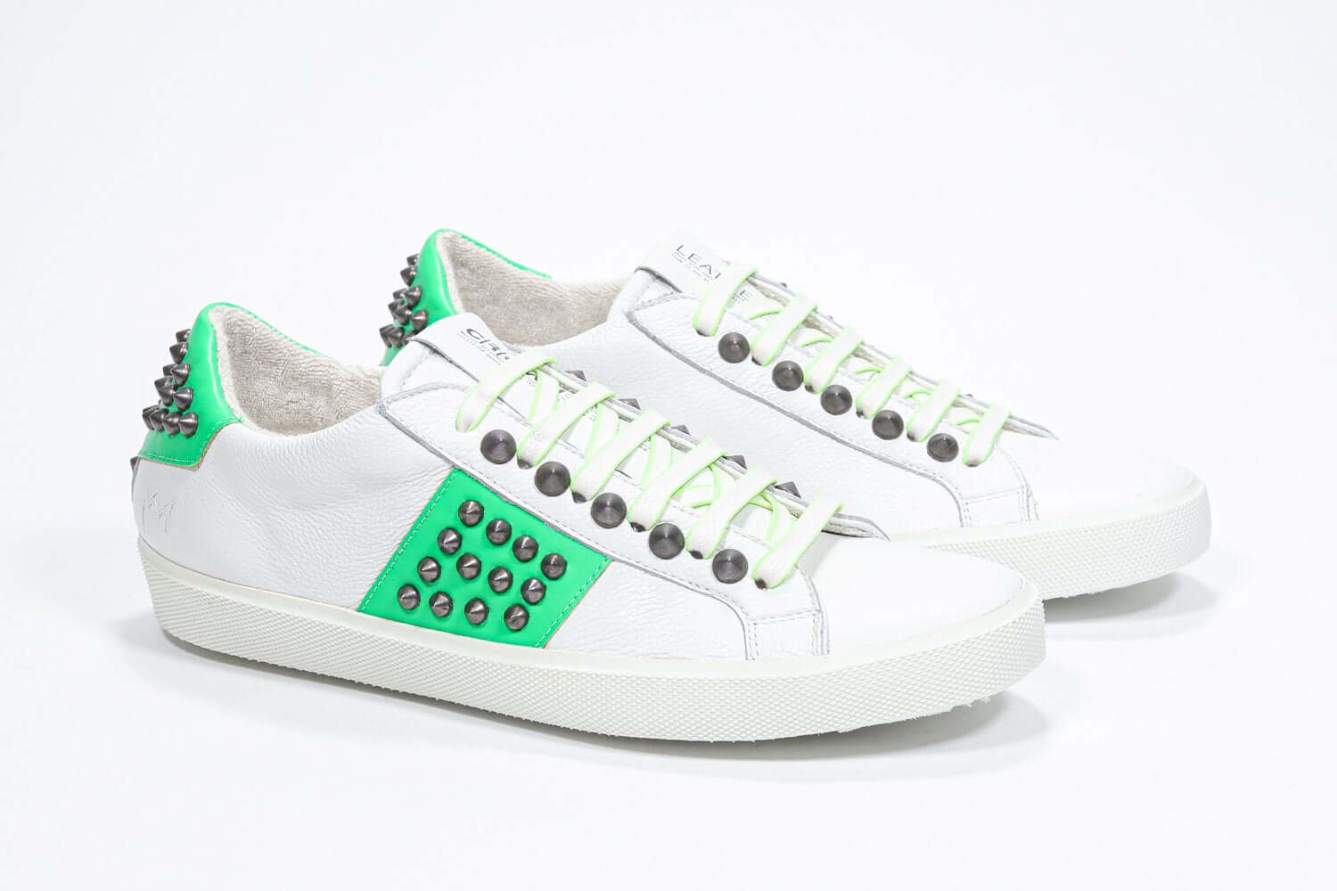 Three quarter front view of low top white and neon green sneaker. Full leather upper with studs and white rubber sole.