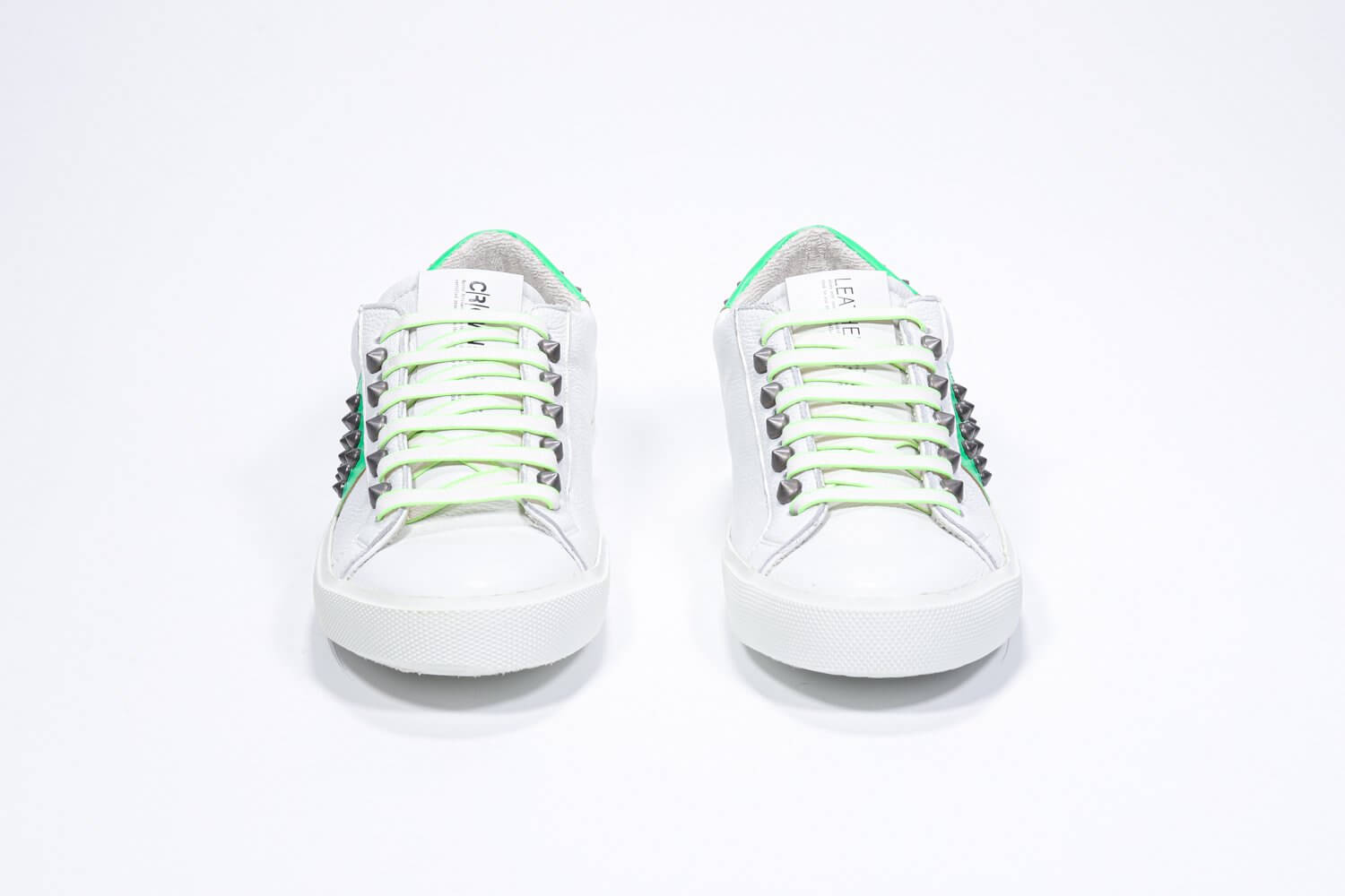 Front view of low top white and neon green sneaker. Full leather upper with studs and white rubber sole.
