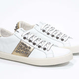 Dreiviertelansicht der Vorderseite von Low Top Weiß und Metallic Gold sneaker. Obermaterial aus Vollleder mit Nieten und Vintage-Gummisohle.