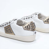 Dreiviertelansicht der Rückseite von Low Top Weiß und Metallic Gold sneaker. Obermaterial aus Vollleder mit Nieten und Vintage-Gummisohle.
