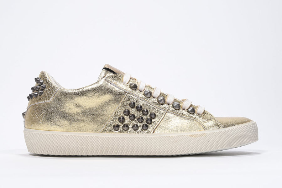 Side profile of low top metallic gold sneaker. Full leather upper with studs and vintage rubber sole.